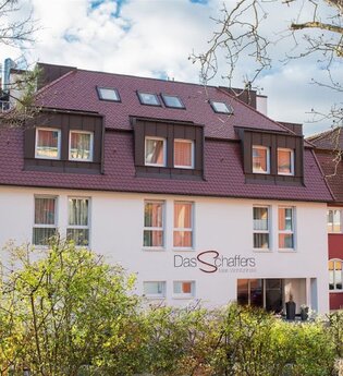 Hotel Das Schaffers mit rotem Dach und weiß-roter Fassade, umgeben von Bäumen und Sträuchern | © Das Schaffers
