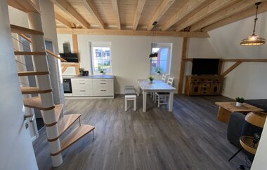 Offener Wohnbereich mit Holzdecke, Wendeltreppe, moderner Küchenzeile, Esstisch mit Stühlen und Fernseher auf Holzkommode | © Ferienwohnung Etzl