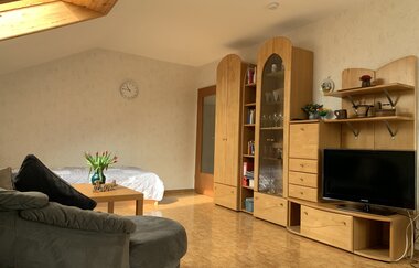 Wohnzimmer mit grauem Sofa, Holzmöbeln, Fernseher, Bücherregal und Tagesbett unter Dachschräge mit Fenster