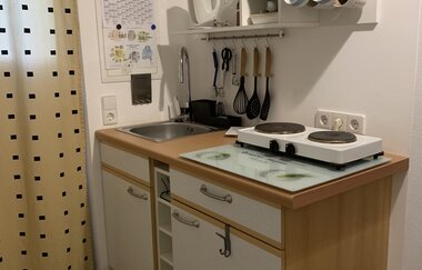 Kleine Küchenzeile mit Spüle, Herd, Küchenutensilien an der Wand und Kaffeemaschine auf der Arbeitsplatte | © Gästehaus Sabine