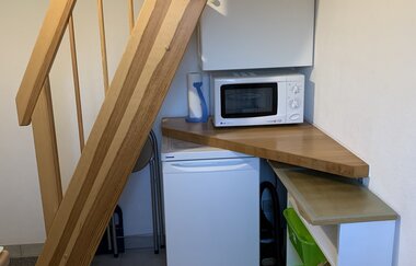 Holztreppe über einer kleinen Küchenzeile mit weißem Kühlschrank, Mikrowelle und schwarzem Wasserkocher | © Gästehaus Sabine