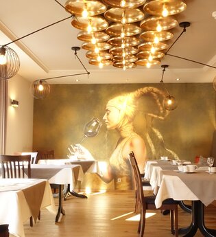 Frühstücksraum mit goldenem Bild von einer Frau im Hintergrund. Rechts gibt es eine Sitzbank mit Kissen und links stehen die Tische am Fenster. | © Neckar-Zaber-Tourismus e.V.