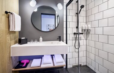 Modernes Bad mit weißen Kacheln, begehbarer Dusche und einem weißen Waschtisch | © Touristikgemeinschaft Hohenlohe e. V. | Moxy Kupferzell Hohenlohe