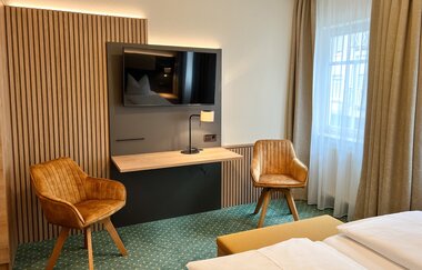 Ein Hotelzimmer mit einem Fernseher an der Wand. Zwei Sessel stehen im Raum. | © Stadthotel Münze