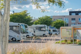 Gepflasterter Stellplatz mit mehreren Wohnmobilen und einer Informationstafel