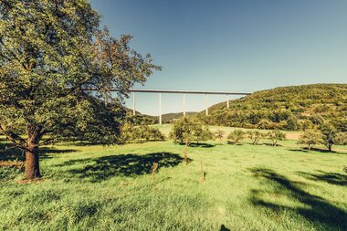 Hier ist die Kochertalbrücke von weiten zu sehen, im Vordergrund kann man sehr viele Bäume und die Natur sehen. | © Arbeitsgemeinschaft Kocher-Jagst-Radweg