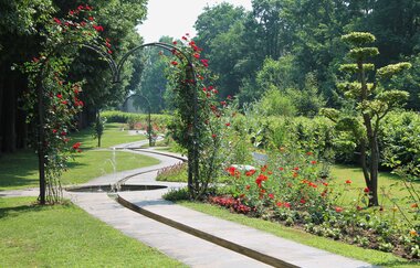 Ein Bachlauf führt durch den Kurpark hindurch. Ein Bogen mit Rosen umwachsen lädt zum durchlaufen ein. | © Kurverwaltung