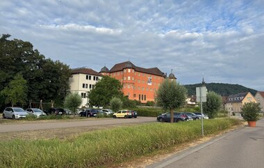 Der Parkplatz liegt unweit des rotgefärbten Schlosses. | © Touristikgemeinschaft Hohenlohe e. V. | Marion Schlund