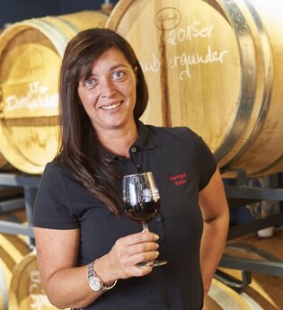 Eine Frau steht mit einem Rotwein vor Weinfässern | © Touristikgemeinschaft Hohenlohe e. V. | Weingut Schneckenhof