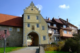 Das Tor ist gelb und hat einen Giebel. Daneben befinden sich Fachwerkhäuser auf der Stadtmauer | © Touristikgemeinschaft Hohenlohe e. V. | Stadt Forchtenberg