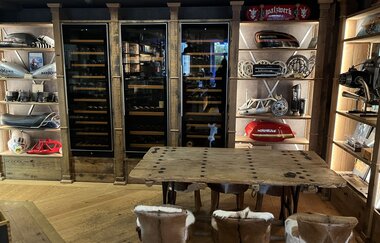Innenansicht des Restaurants mit rustikalen Holzmöblen, Weinregal und Motorradteilen und einem Tisch mit niedrigen Stühlen, die einen Überzug aus Fell haben. | © Walzwerk Schwetzingen