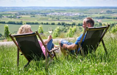 Zwei Personen sitzen im Liegestuhl und genießen ihren Wein mit Aussicht vom Biergarten Heuchelberger Warte. | © Touristikgemeinschaft HeilbronnerLand