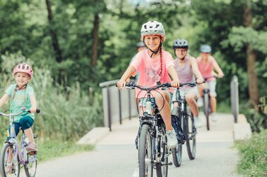 Ein großes und ein kleines Mädchen fahren Fahrrad. Im Hintergrund sind zwei weitere Menschen auf dem Fahrrad zu sehen. | © Touristikgemeinschaft HeilbronnerLand
